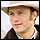 Pixelated static image of a person wearing a light-colored wide-brimmed hat and dark clothing with white collar, set against a pale background.