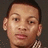 Pixelated close-up of a person's face with short dark hair, light skin, and a checkered shirt collar visible against a dark background.