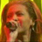 Pixelated static image of a person with long hair and red facial highlights against a yellow-green gradient background, rendered in low-resolution 256x256 pixels.