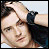 Static pixelated image of a person with light skin tone, dark hair styled in an updo, and wearing a black bow on the right side of their head.