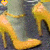 Animated sequence of a woman's legs in gray tights and yellow high-heeled shoes, with small orange hearts floating upward.