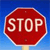 Red octagonal sign with white text reading STOP on a blue gradient background, mounted on a light brown pole.