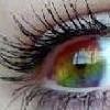 A close-up of a human eye with long dark eyelashes, a colorful iris showing red, yellow, green, and blue hues, and visible skin texture around the eye.