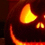 A carved pumpkin face with glowing orange eyes and mouth against a dark background, showing subtle animation changes.