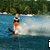 A person water skiing on blue water with green trees in the background, shown across with text overlays