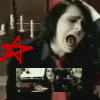showing a person with dark hair in a black jacket and red shirt, mouth open wide as if shouting or singing, overlaid with red star symbols