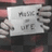 A hand holds a white paper with handwritten text against a dark background with red accents.