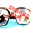 Pixelated sunglasses with red floral patterns on lenses, resting on a light blue surface against white background.