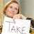 A pixelated image shows a person with light brown hair holding a white sign with the word "TAKE" in gray letters, positioned against a blurred background.
