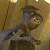 Pixelated static image of a character in military attire with a hat, holding an object near their face against a warm-toned background.