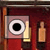 Pixelated static image shows a square icon with a central black circle surrounded by white rings on a pinkish background, next to a yellow rectangular shape and a light brown vertical shape against a dark red backdrop.