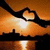 Silhouetted hands form a heart shape against an orange sunset sky with water reflection below.