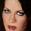 Pixelated close-up of a person's face showing eyes, nose, mouth with red lips and dark hair against black background.
