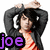 A person with dark hair and a black jacket over an orange striped shirt holds both hands behind their head in a static pose