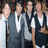 Four individuals in formal attire stand side-by-side against a blurred background with warm tones.