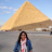 A pixelated image shows a person standing in front of a large pyramid under a clear blue sky with scattered clouds.