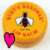 A pixelated circular icon with a yellow-orange gradient background, featuring a stylized face with closed eyes and a small mouth, plus a bright pink heart symbol on the left side.