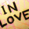 Static image with bold black text reading 'IN LOVE' on a yellow background with pink and orange streaks.