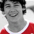 A person in a red shirt with white collar smiling broadly, shown in four -like with varying grayscale tones