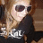 A pixelated image of a person with long light brown hair wearing dark sunglasses and a black top, with text below the figure.
