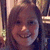 Pixelated close-up of a smiling person with brown hair, wearing dark clothing against a blurred background.