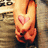 A person's hands clasped in front of their chest with a pink heart symbol on the left hand, wearing a gray long-sleeve shirt and dark pants.