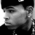 Pixelated grayscale portrait of a person with short hair, wearing a dark cap and dark clothing, viewed in profile from the left side.