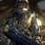 Animated metallic figure in armor with reflective surface, holding a dark blue object against brown background.