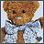 Brown teddy bear with black eyes and white nose wears light blue shirt, standing against light background.