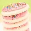 Stacked pink and white layered cake with colorful sprinkles on top against a light green background.