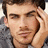 Pixelated close-up of a person with short brown hair, light skin tone, and visible facial features including eyes, nose, mouth, and ear.