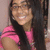 A person with long dark hair and glasses wears a pink shirt, smiling broadly in three showing slight head movement