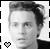 Black-and-white pixelated portrait of a person with short hair, wearing dark clothing and featuring a small heart symbol in the bottom-left corner.