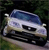 Pixelated image of a white car with blue roof on dark background, viewed from front-left angle with visible headlights and grille.