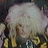 Pixelated static image of a figure with light-colored hair and dark clothing against a muted background.