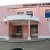 Pixelated static image of a two-story building with pink and beige walls, dark windows, and a light blue balcony railing.