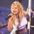 Animated sequence of a woman with long blonde hair singing into a microphone, wearing a white and pink outfit against dark background.