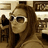Pixelated static image of a person with long brown hair wearing dark sunglasses and a light-colored top, set against a blurred background with indistinct shapes.