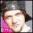 Pixelated portrait of a person with closed eyes, wearing dark hair and light clothing against pink-and-white checkered background.
