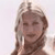 Pixelated image of a person with light brown hair styled in two braids, wearing a dark strap across the chest, against a light background.