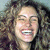 A pixelated close-up of a person with curly hair, showing a wide smile with visible teeth and closed eyes.