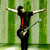A person in a black shirt with red stripe and dark pants holds a guitar, arms outstretched against green-and-white striped background; text appears below.