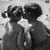 Two children in dark dresses stand side-by-side facing left, their hair styled with bows; the right child's dress has a white star on the back.