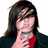 A person with long dark hair and a red shirt under a black jacket poses with a hand near their chin against a white background, next to a red with teal text