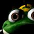 Pixelated close-up of a green cartoon frog face with large eyes and yellow accents on its head against a black background.