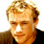 Static pixelated image of a person's face with light brown hair and dark clothing against a white background.