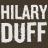 Pixelated text displays 'HILARY DUFF' in large white block letters on a dark brown background.