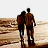 A pixelated image showing two figures walking away on a beach with text asking if they can stay in each other's arms.