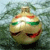 A pixelated spherical object with green and red accents, a brown top, and a wide red smile against a blurred green background.