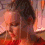 A four- shows a person with dark hair tied up, wearing a red top, against a warm-toned background with vertical elements